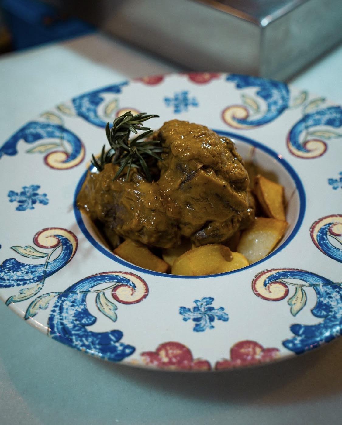 Guiso de carne con patatas y una ramita de romero, en plato de cerámica azul y blanca